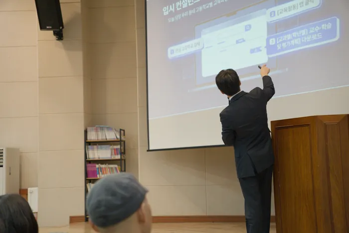 강단에서 발표자가 스크린에 띄운 화면을 가리키며 설명하는 모습