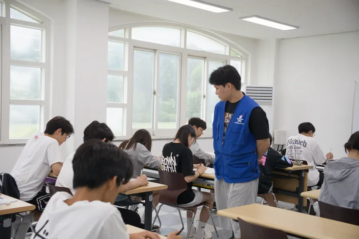 조끼를 입은 담당자가 자습실 안쪽에 서서 학생들의 진행 상황을 살피는 모습
