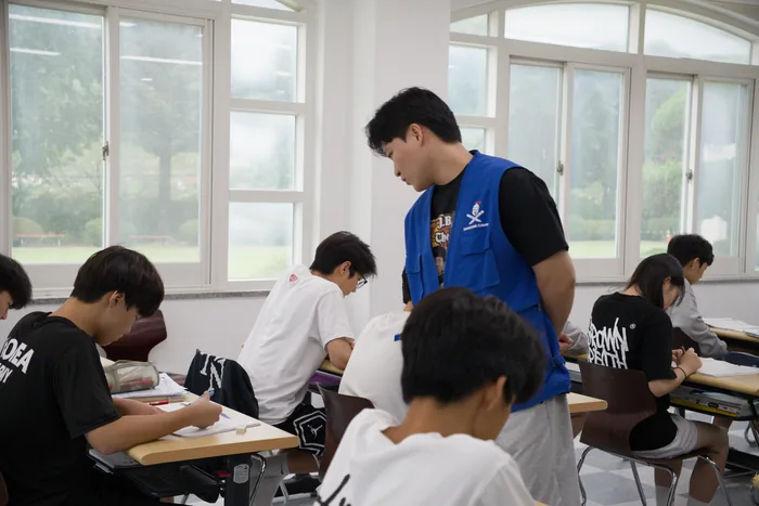 창가 자리에서 담당자가 학생이 풀고 있는 문제를 들여다보는 모습