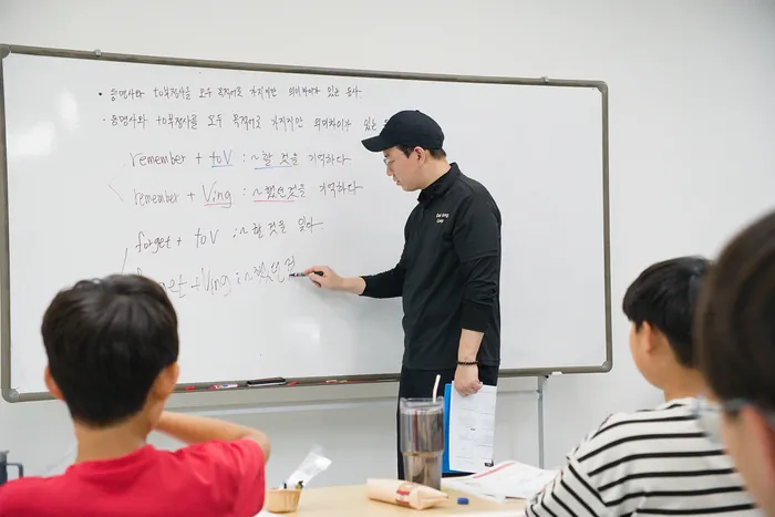 선생님이 화이트보드에 영어 문법 예문을 적으며 수업하는 모습